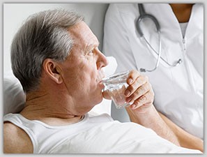 Nurse tending to elderly man as he lays in bed and sips water